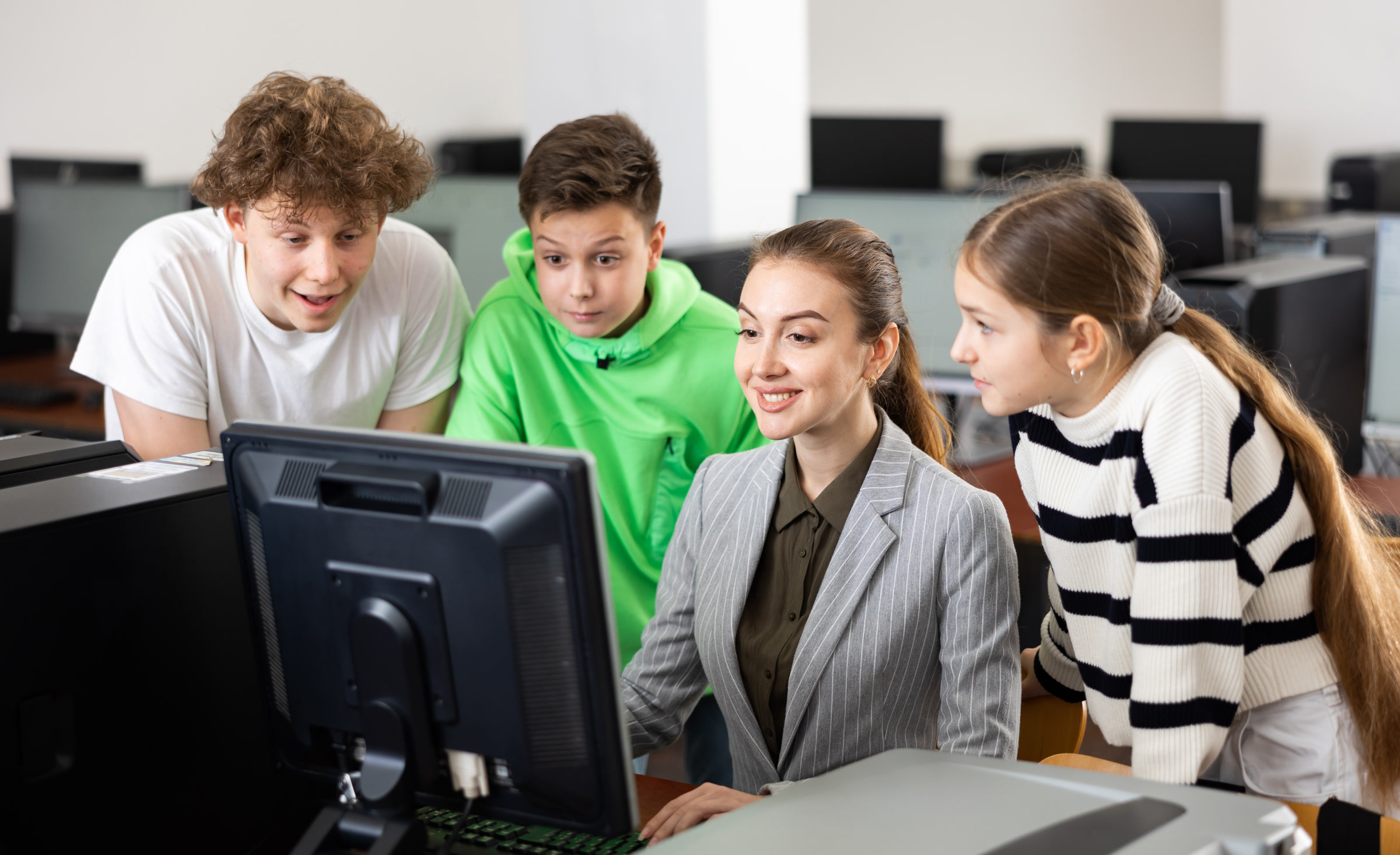 Female teacher helping schoolboy and schoo lgirl in computer class
