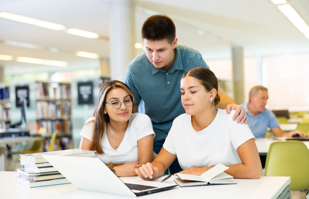 Friendly happy group of students preparing together for exam in university library