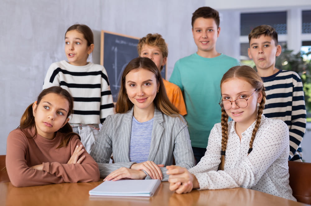 Portrait of positive group of pupils with female teacher sitting in schoolroom