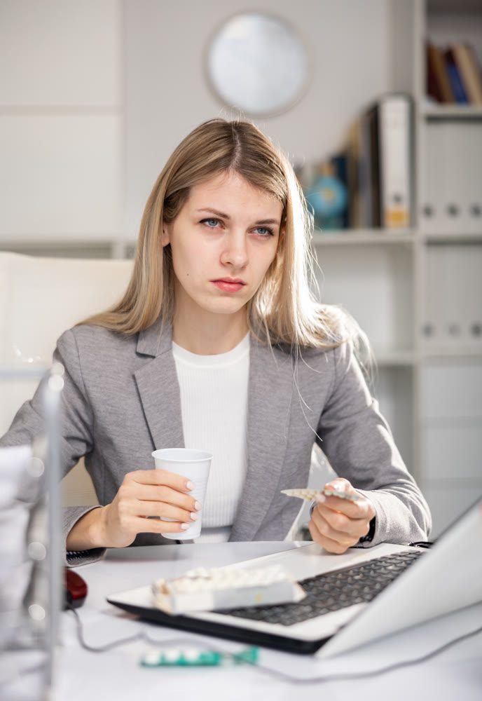 Tired business woman drinking headache pills in office