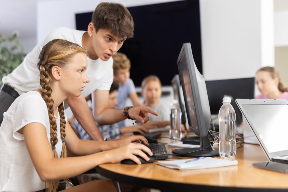 Preteen girl learning computer programs with teacher in training room