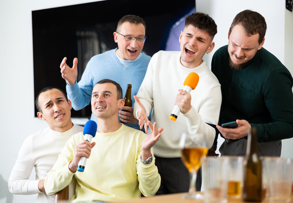 Cheerful men at bachelor party with karaoke and drinks at home