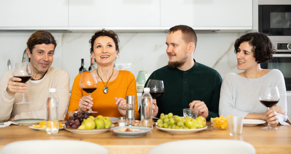Two married couples are sitting at table, enjoying food and wine, chatting, talking, laughing.