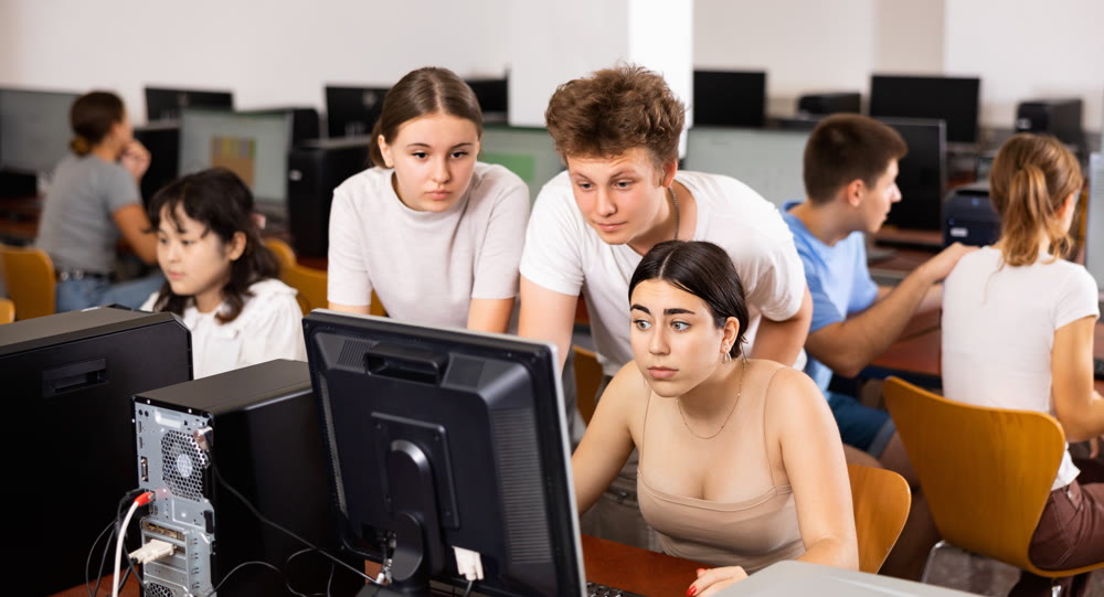 Portrait of multinational young students group emotionally reacting while studying at pc in computer class