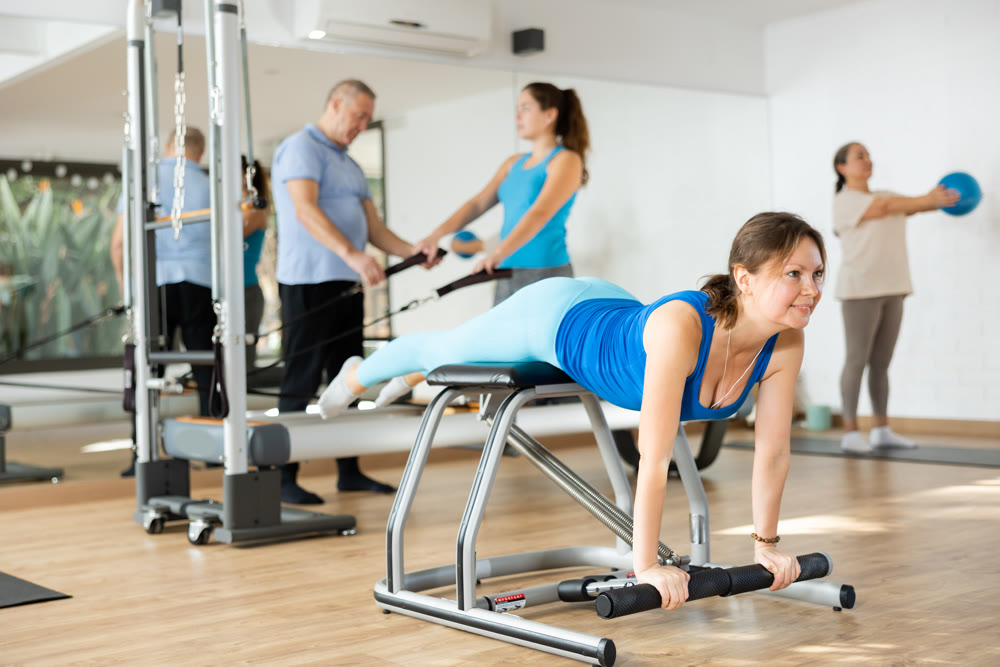 Middle-aged woman practicing pilates on pedal fitness chair in sports hall