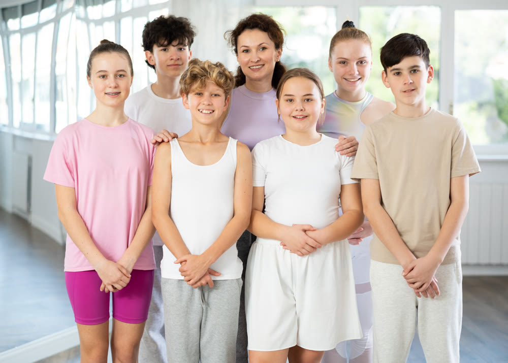 Group portrait of cheerful teenage dancers in row in choreographic studio