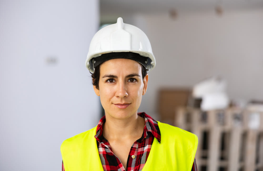 Portrait of positive builder woman in vest and safety helmet