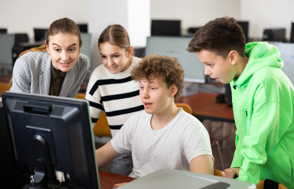 Female teacher helping schoolboy and schoo lgirl in computer class