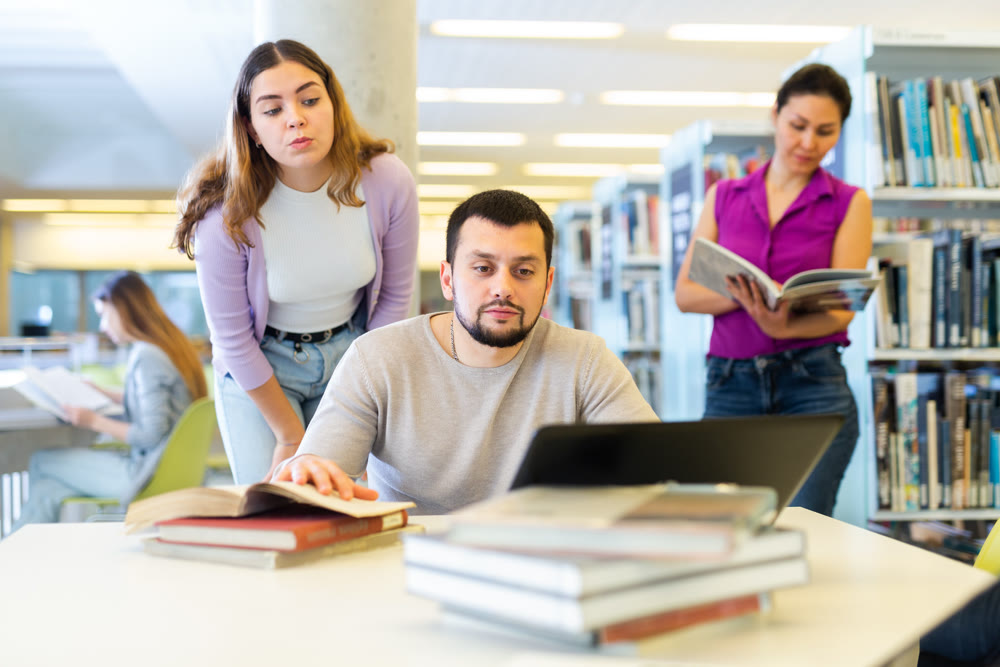 Student girl in the library peeps into the monitor of a guy classmate