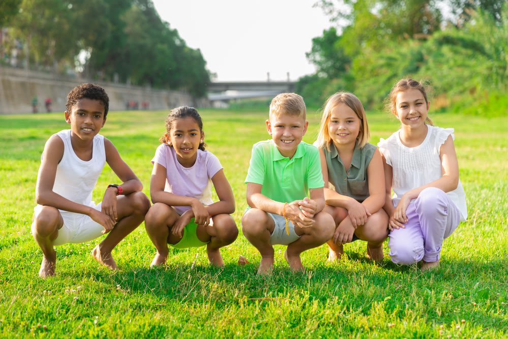 Multiracial group of cheerful preteen friends posing on green lawn