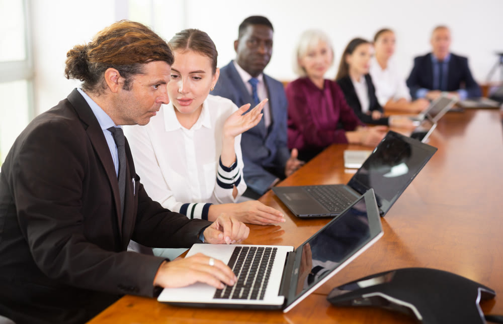 Mid-aged white businessman co-working on laptop with his young female colleague at office
