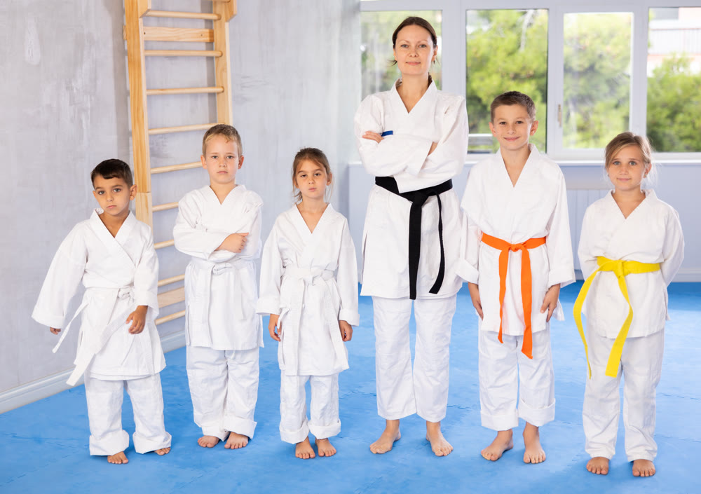 Team of young martial arts athletes is standing in gym with female coach.