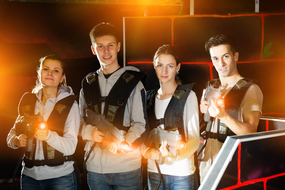 Happy young people with laser pistols posing together in bright beams in laser tag labyrinth
