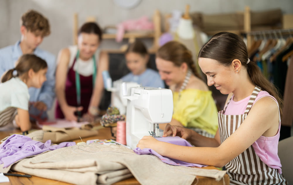 Engaged teenage schoolgirl stitching fabric on machine in sewing class