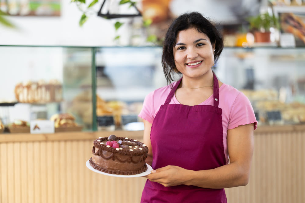 Positive young seller demonstrating cake in cafeteria