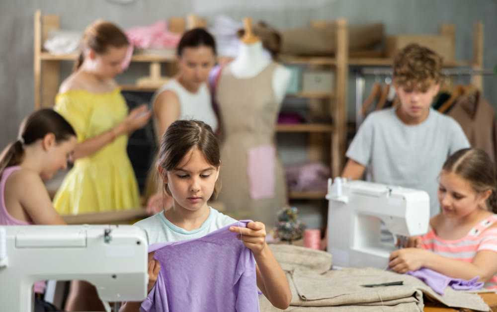 Little girl checking stitched fabric at school sewing workshop