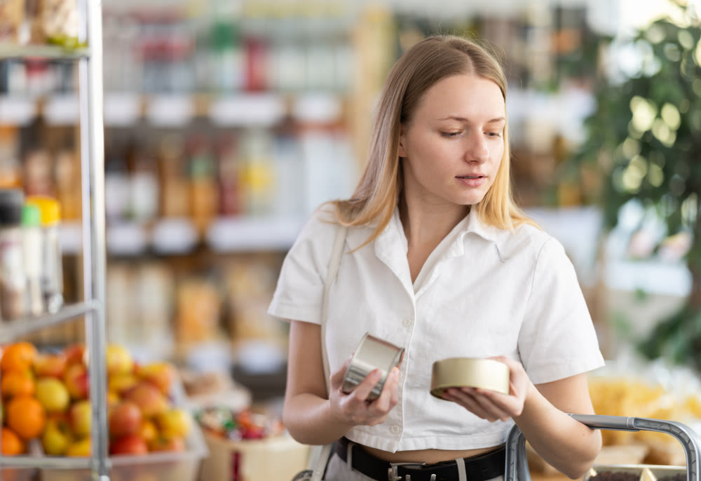 Young woman choosing canned food in grocery store