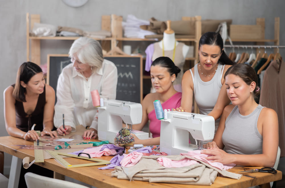 Group of busy women sewing and drawing with teacher at dressmaking courses