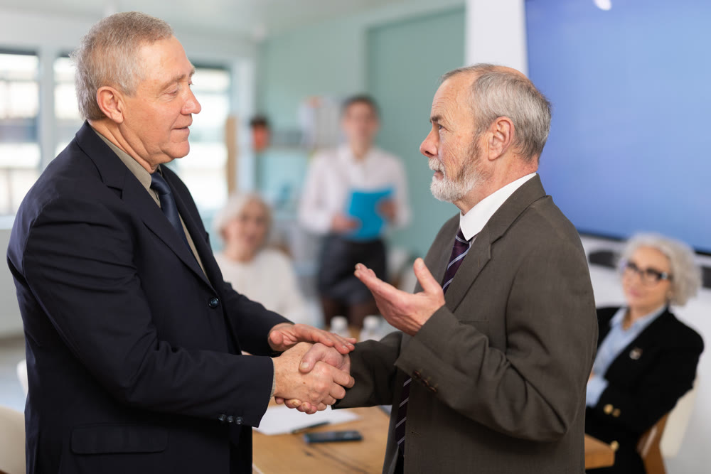 Senior men participants of meeting end business negotiations with handshake