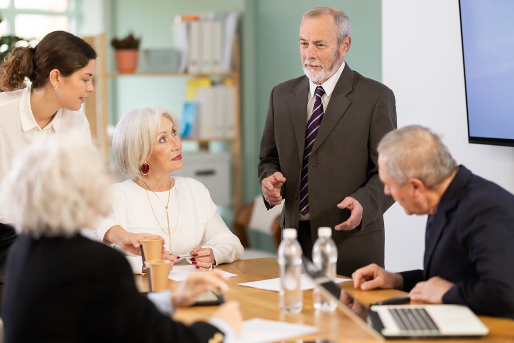 Elderly man leading meeting with senior colleagues at table