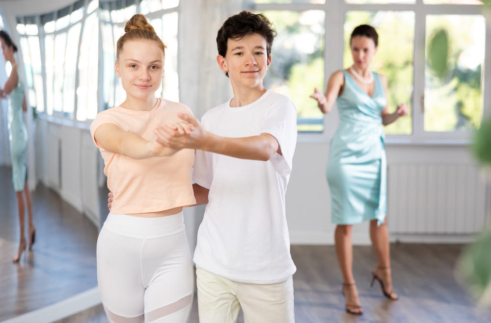 Teenage girl and boy practicing waltz in dance hall with female mentor