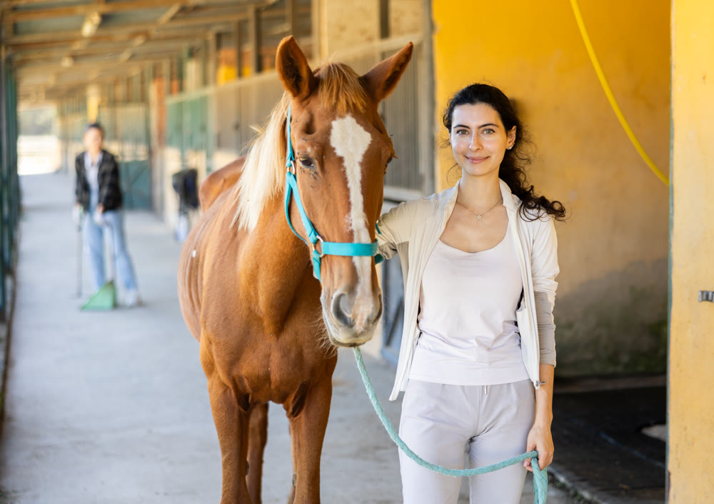 Young woman leads horse out of stable