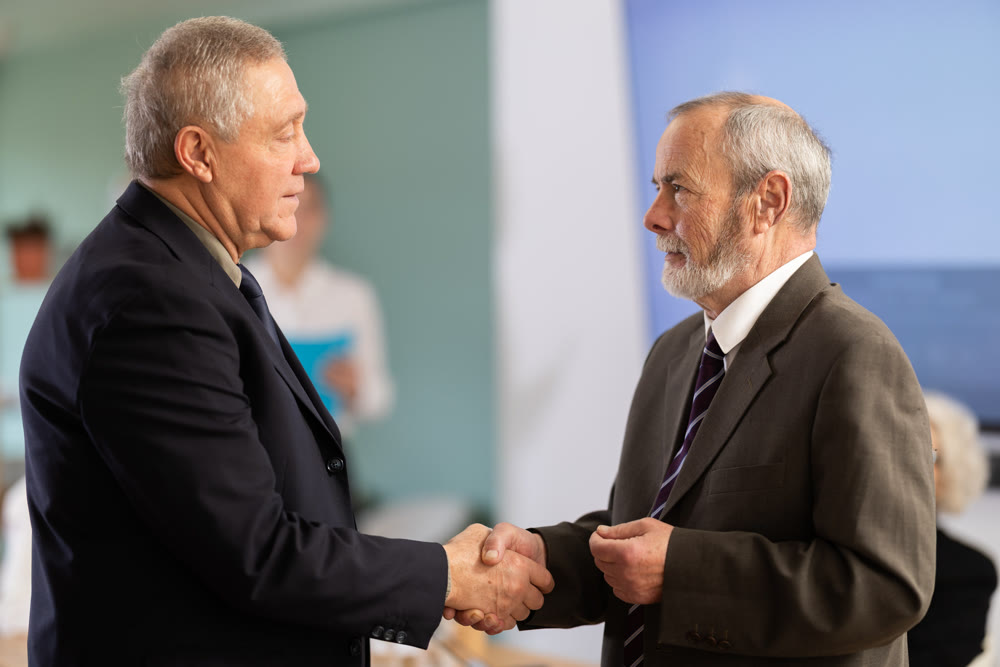 Senior men participants of meeting end business negotiations with handshake