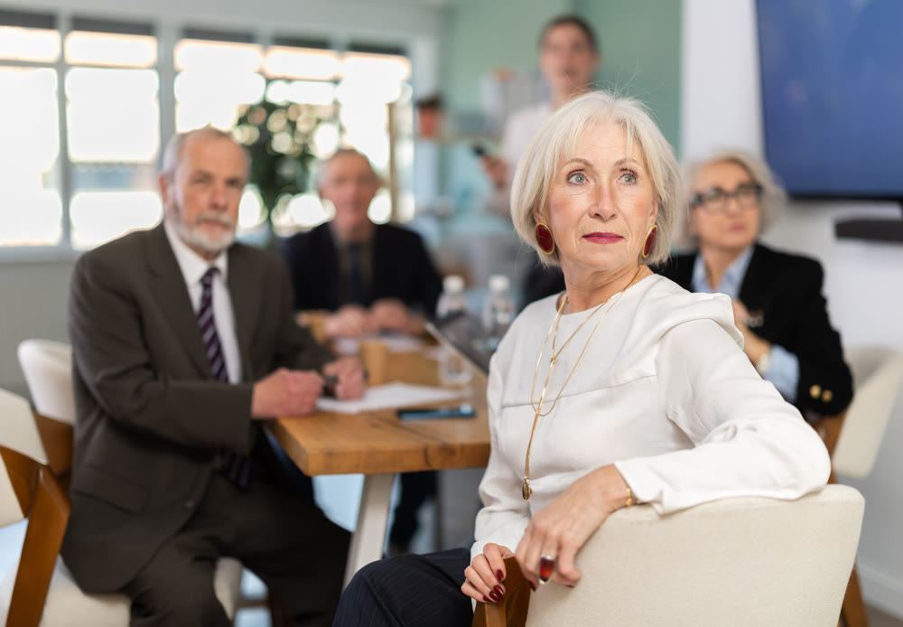 Elderly woman in group watches presentation given by young secretary