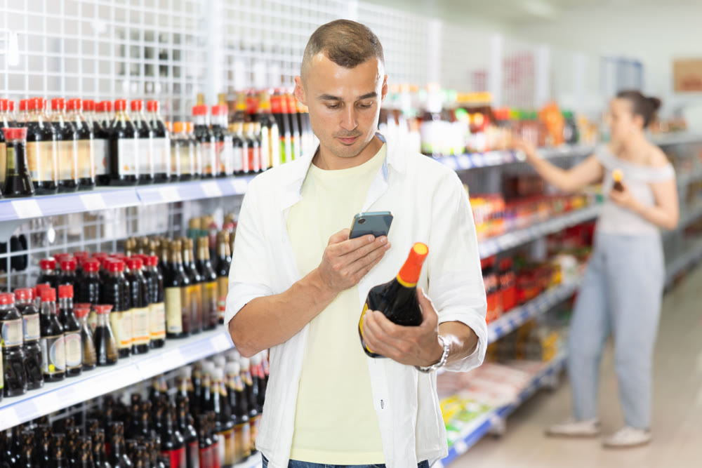 Young man using smartphone to scan barcode on soy sauce in store
