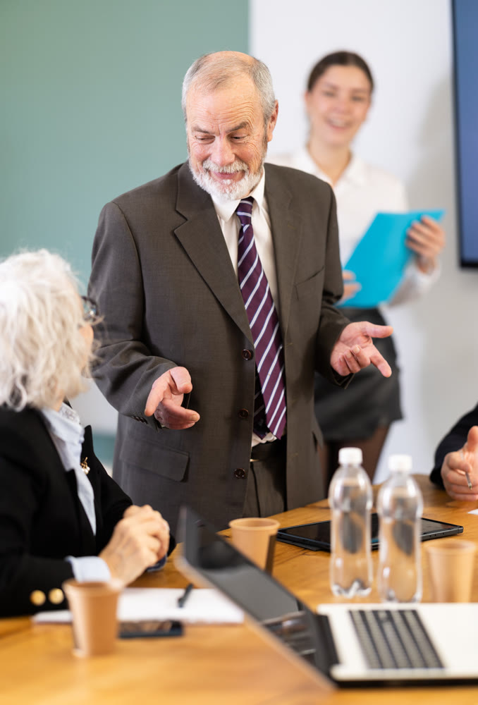 Senior male speaker shares happy news, makes participants laugh