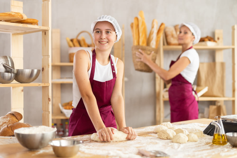 Two women prepare dough and take hot baguettes out of the oven - work in bakery