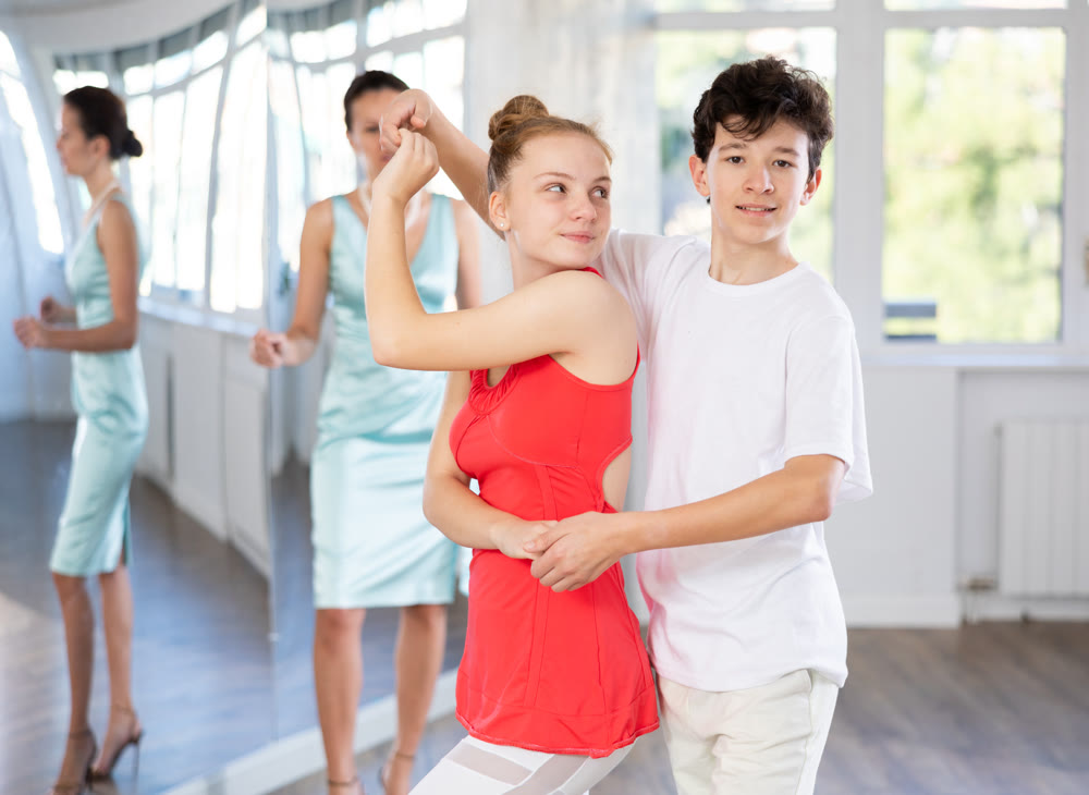 Experienced dance teacher teaching ballroom dancing to a couple of teenagers in studio