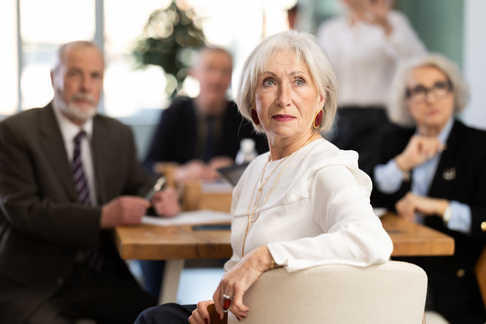 Elderly woman in group watches presentation given by young secretary