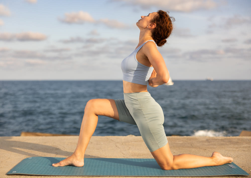 Yoga practice on embankment, female athlete fulfil carry out Anjaneyasana