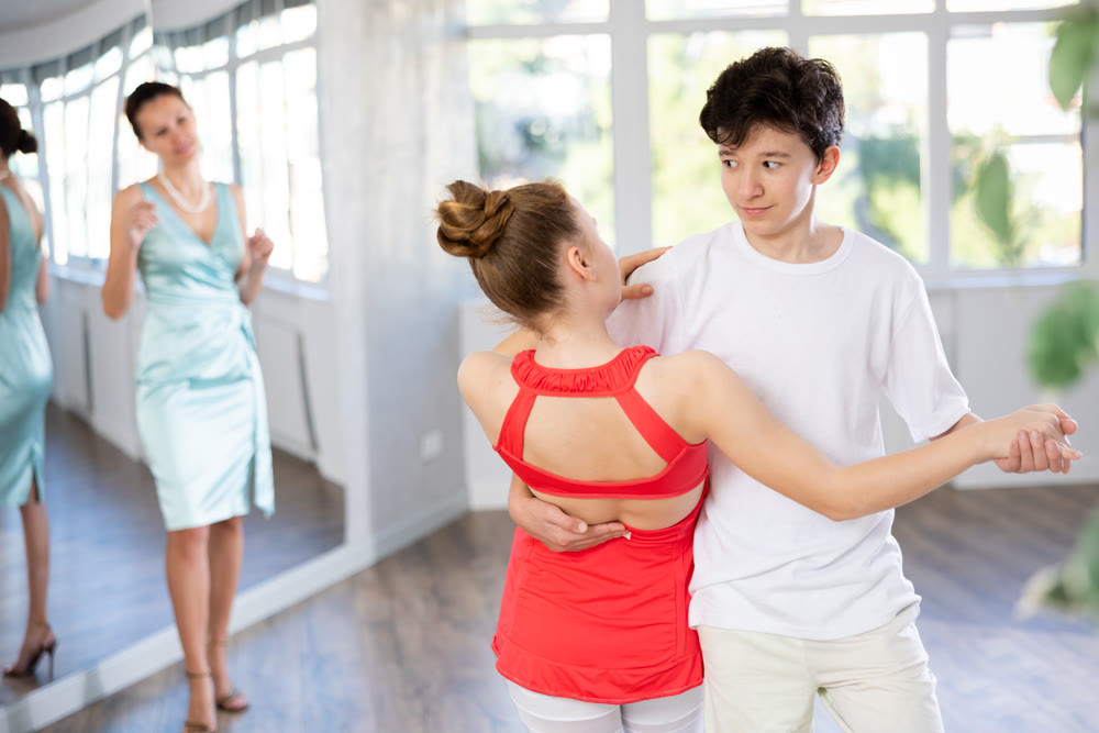 Teenage girl and boy practicing waltz in dance hall with female mentor