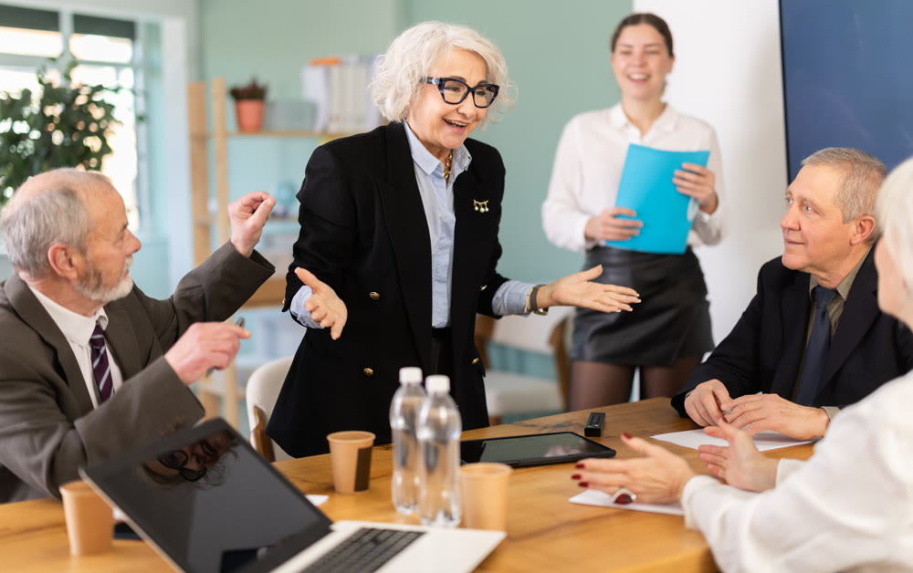 Senior female speaker shares happy news, makes participants laugh