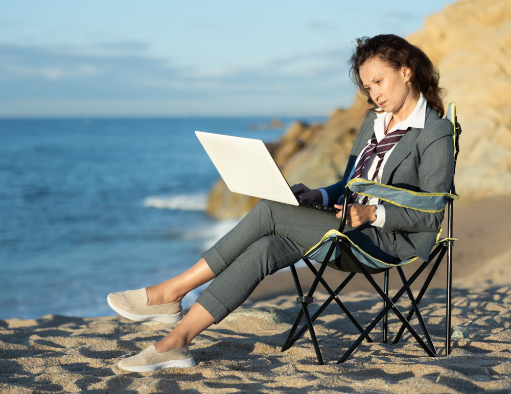 Businesswoman in office clothes working on laptop on seashore