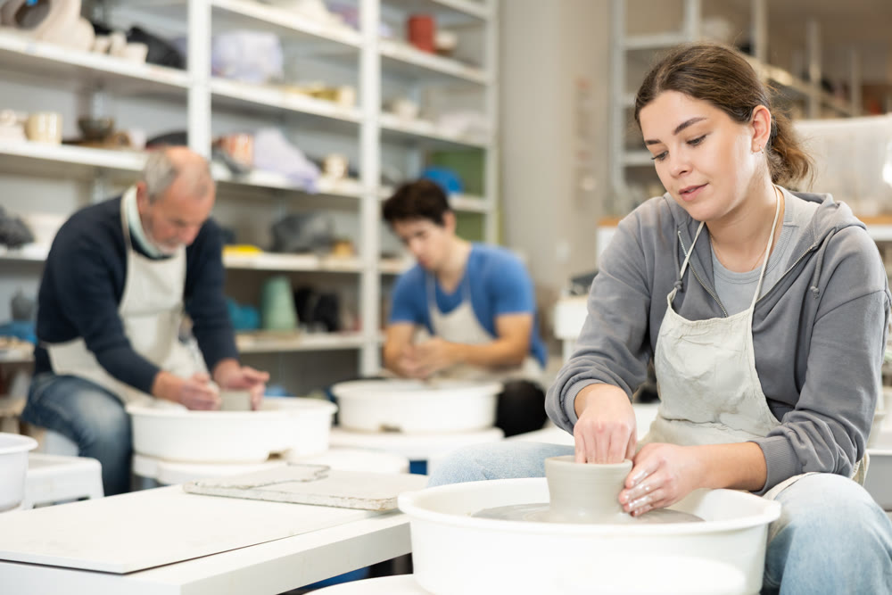 Young woman shaping pottery on wheel in ceramics studio