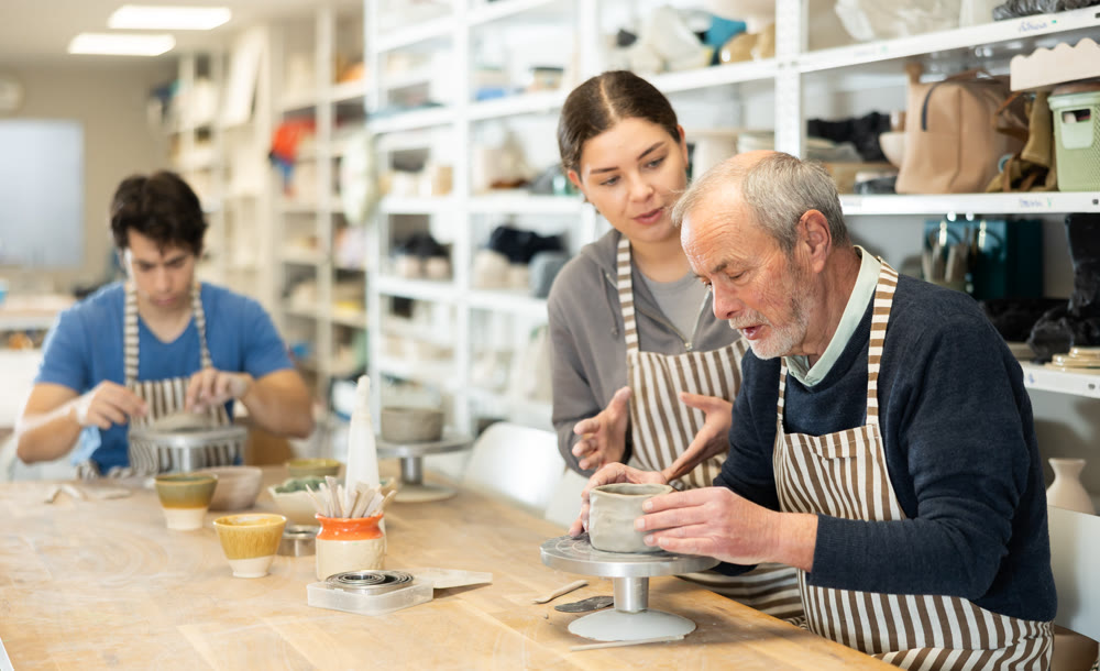 Young woman helping eldery man sculpting ceramic piece