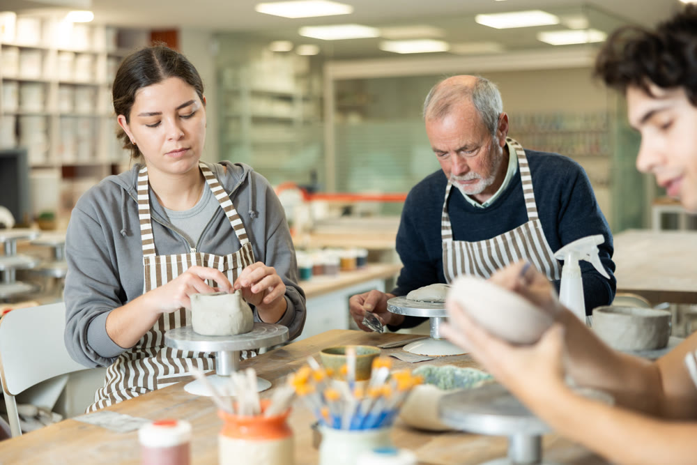 During working day, three pottery workshop workers sculpt from clay, form final product