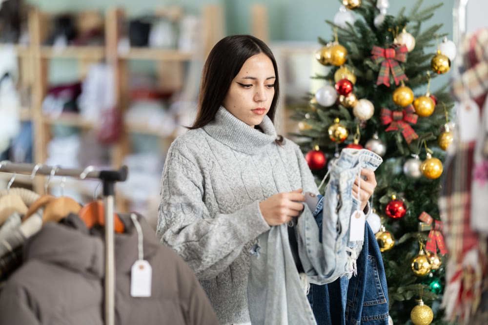 Brunette woman stands against of the Christmas tree and chooses jeans