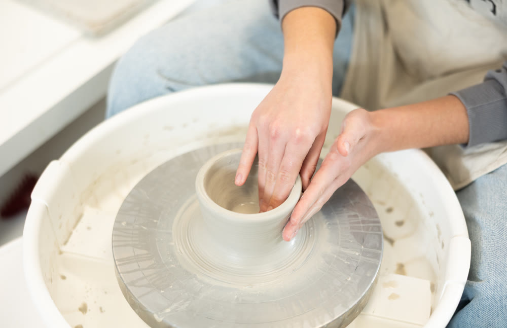 Close-up of woman's hands shaping clay on pottery wheel