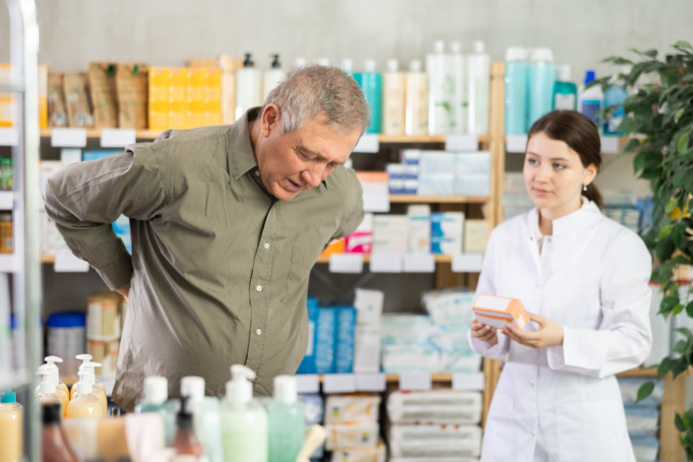 Senior man visits pharmacy and suffers from backache. Girl pharmacist offer help