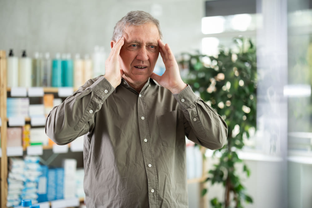 Senior man with headache looking for medicine in pharmacy