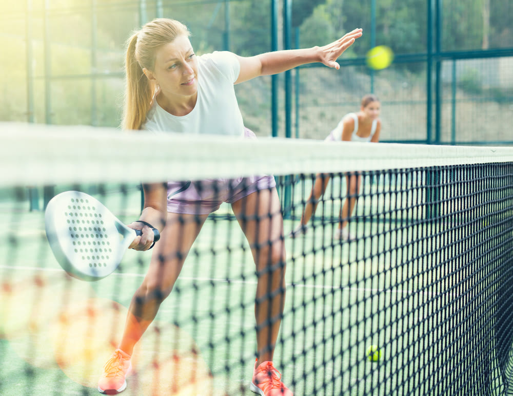 Athletic caucasian woman plays padel. View through tennis net