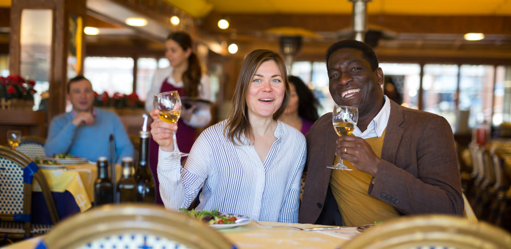 Cheerful woman with african american friend having dinner in restaurant