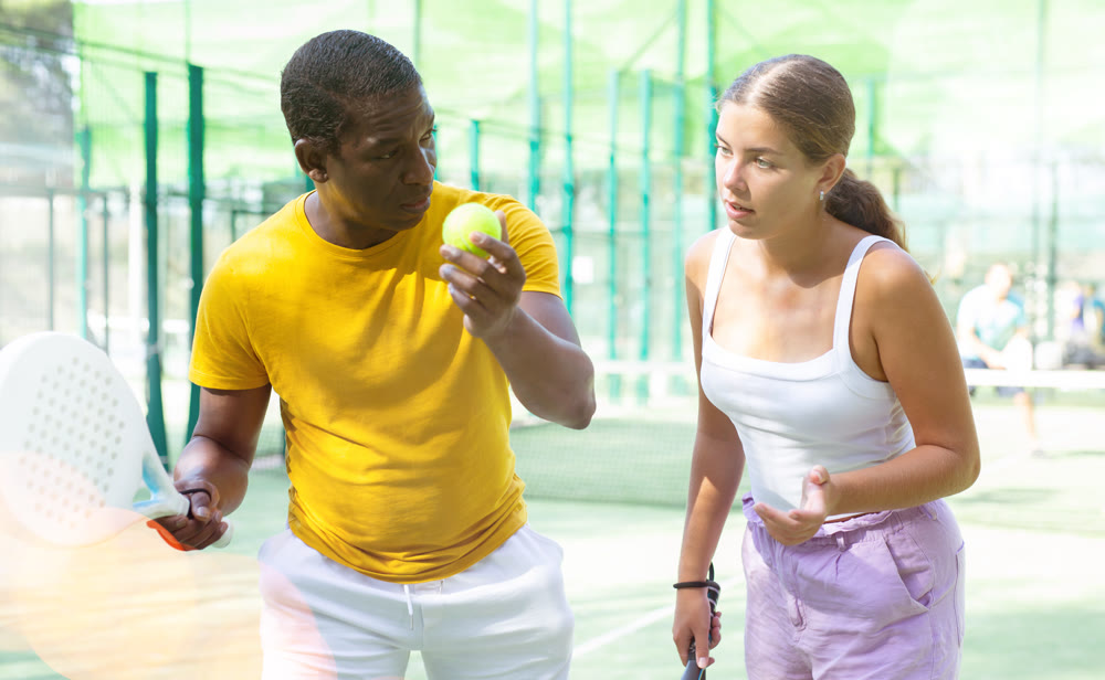 African american man instructor teaches a young woman to play padel tennis