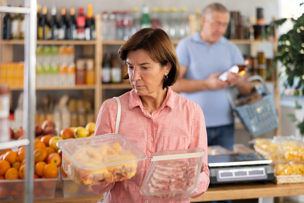Woman chooses chicken or pork fillet, while her husband buys alcohol in supermarket