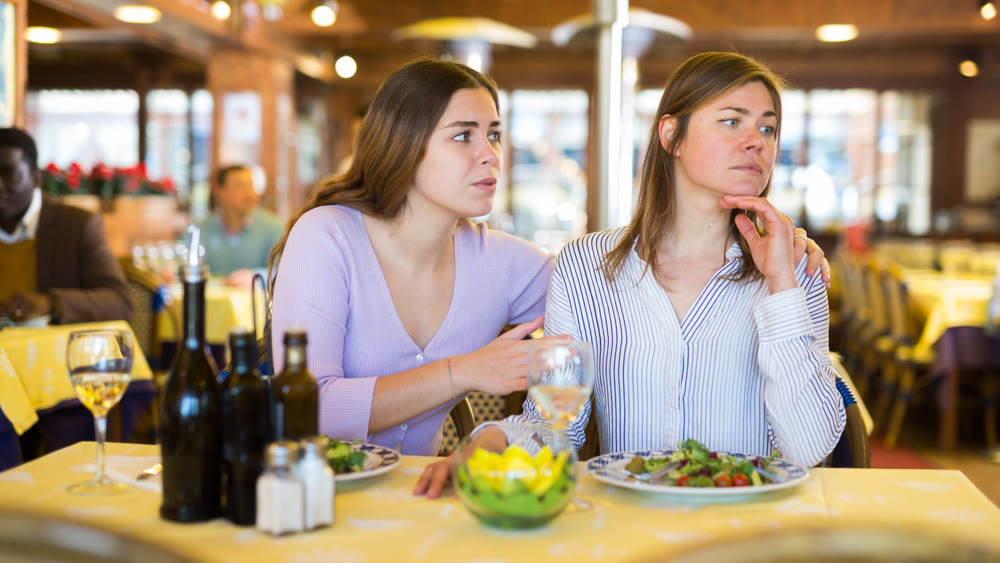Woman calming upset female friend in restaurant during dinner