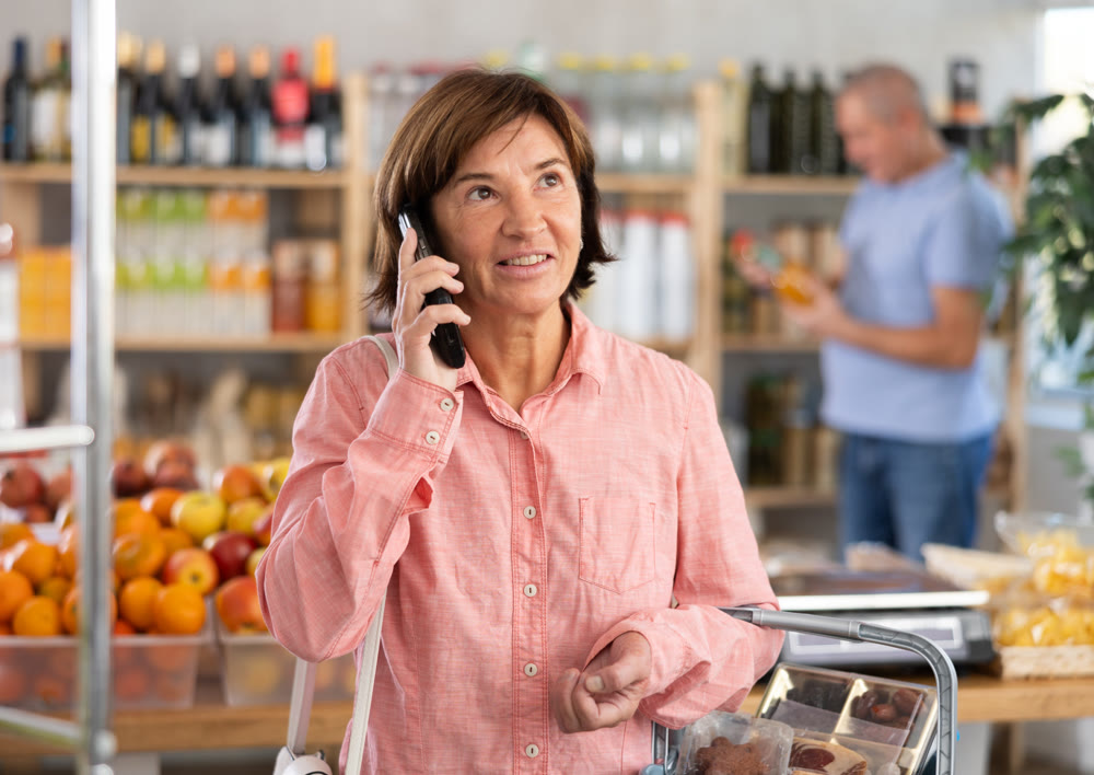 Woman shopper is talking on mobile phone while her husband is shopping in produce section of supermarket